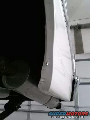 White car fender with chrome trim and visible exhaust pipe, viewed from below