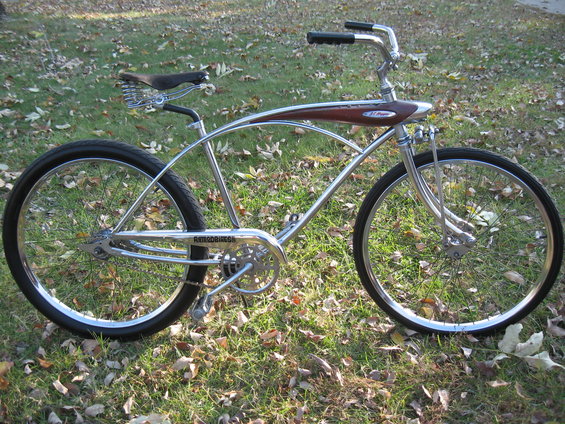 Chrome cruiser bicycle with brown wood-grain tank and black grips, parked on grass with fallen leaves