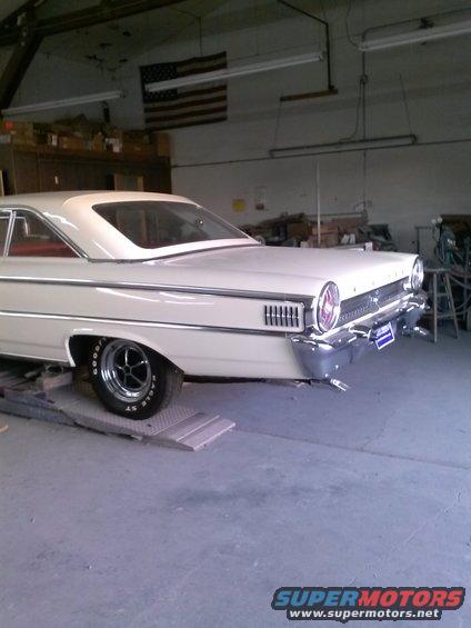 Rear quarter view of a white 1961 Ford Galaxie parked in a garage. American flag hangs on the wall