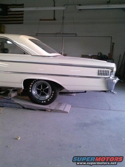 Cream-colored 1963 Ford Galaxie rear quarter panel on ramps, showing chrome trim, horizontal taillights, and a "SuperMotors.net" watermark