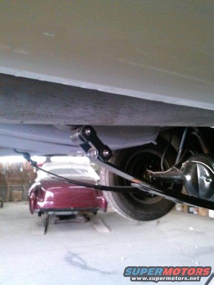 Rear suspension and leaf spring on a classic car, with a red coupe visible in the background