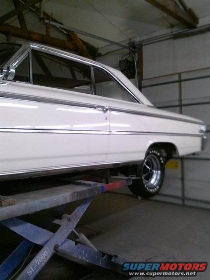 White 1964 sedan on a lift, side view. Shows chrome trim and a Goodyear Eagle GT tire
