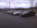 2003 Ford Crown Victoria - A line of sedans, including a black 2003 Ford Crown Victoria, are parked in a lot under an overcast sky.