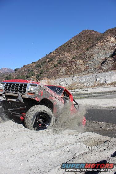 Red 1978 Ford Bronco off-roading through sand, kicking up dust