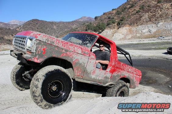 1978 Ford Bronco in red, mud-splattered, with large tires, off-roading