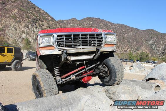 red off-road SUV with large tires on rocks, yellow Jeep and other vehicles in background