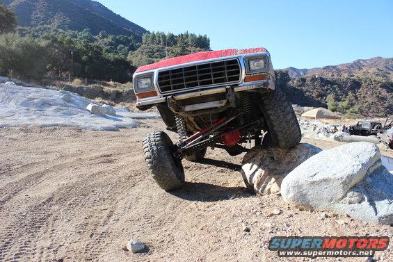 Red 1978 Ford Bronco climbing over rocks on a dirt trail
