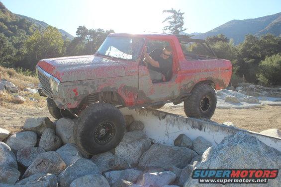 1978 Ford Bronco climbing over a rock obstacle, covered in mud