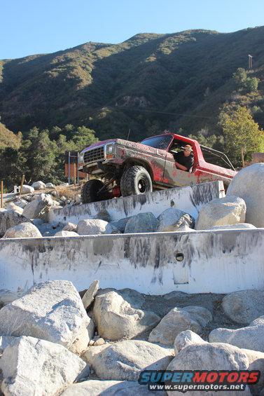 red off-road truck climbing over rocks, driver visible