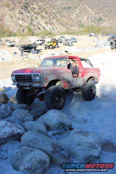 Red 1978 Ford Bronco with large tires navigating rocky terrain