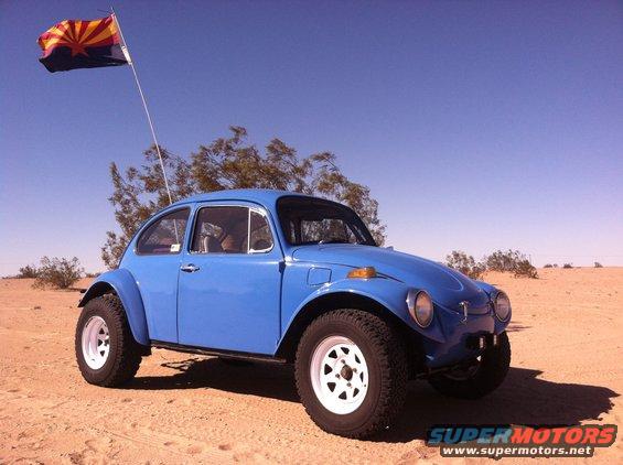 Blue Volkswagen Beetle Baja Bug with off-road tires and white rims, Arizona flag flying, parked in desert