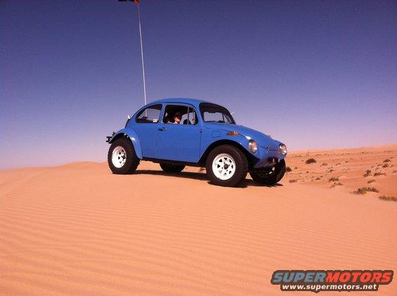 Blue 1970 Volkswagen Beetle Baja Bug driving on sand dunes with a flag