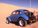 1970 Volkswagen Beetle - A blue dune buggy sits on a sandy terrain under a clear blue sky, with its engine exposed at the rear.