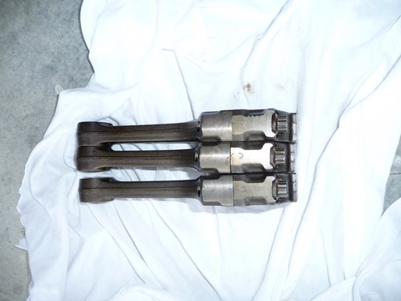 Three engine connecting rods laid out on white cloth. Some have numbers like '3' and '5' stamped on them