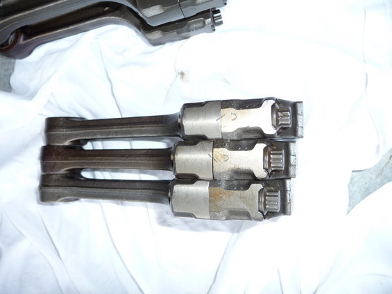 Three engine connecting rods stacked on a white cloth. Some have numbers marked on them