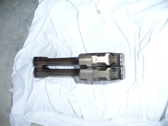 Two engine connecting rods with toothed caps, laid on white cloth