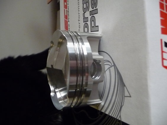 Close-up of a shiny metal piston with rings, next to a box with text