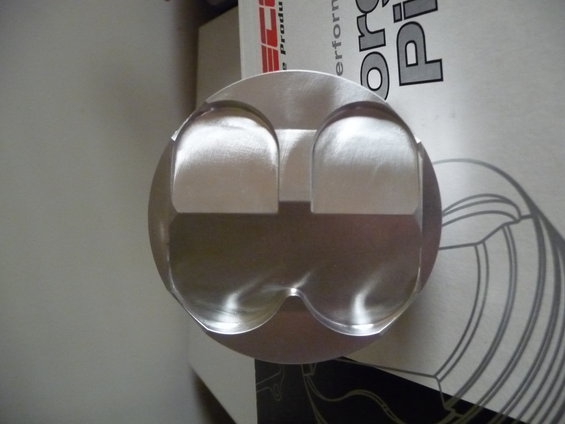Piston with two valve reliefs and a domed top, resting on packaging with text