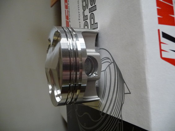 Wiseco piston with multiple compression ring grooves, resting against a box with graphics