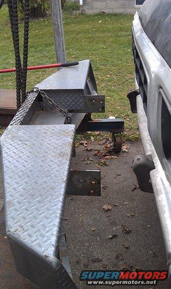 Diamond plate bumper attached to a trailer hitch, with a vehicle grille visible to the right