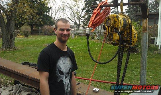 Man in skull shirt standing next to yellow hoist with orange cord