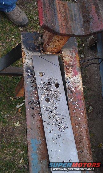 Metal plate with three drilled holes and metal shavings on a rusty metal surface