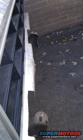 Metal front bumper section with cutouts and tow hook mounts, next to a black grille