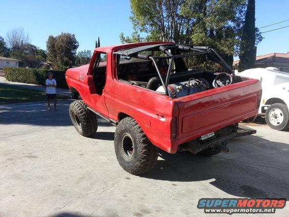 Red 1978 Ford Bronco with roll cage and large tires, rear view