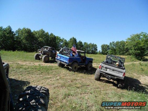 Blue Ford Bronco with American flag, gray Ford Bronco, and off-road buggy on a sunny day