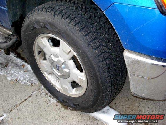Blue Ford F-150 front wheel with a winter tire, chrome bumper visible