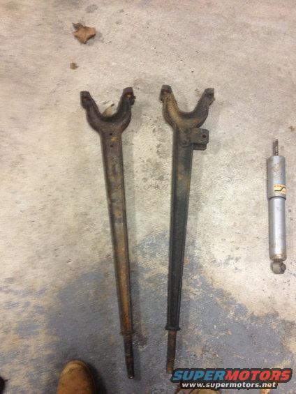 Two rusty control arms and a silver shock absorber lie on a concrete floor