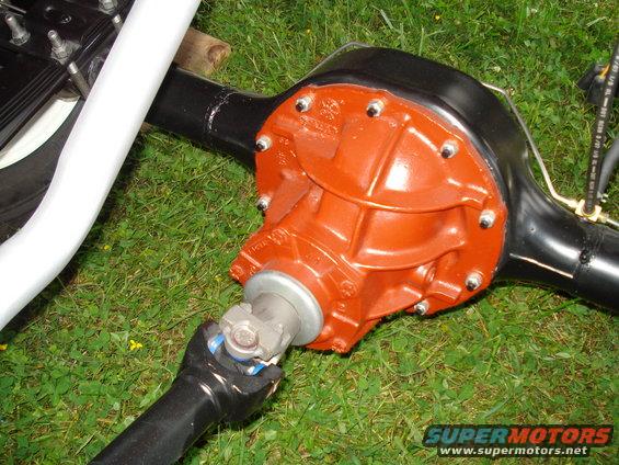 Close-up of a rear axle assembly with an orange differential cover and black housing, connected to a driveshaft