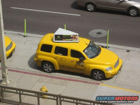 Yellow taxi with 'Yellow Cab' logo and phone number on the side. Another yellow vehicle is partially visible to the left
