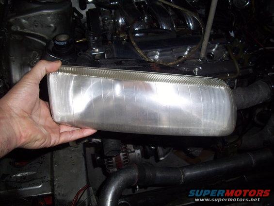 Hand holding a clear headlight assembly in front of a car engine bay