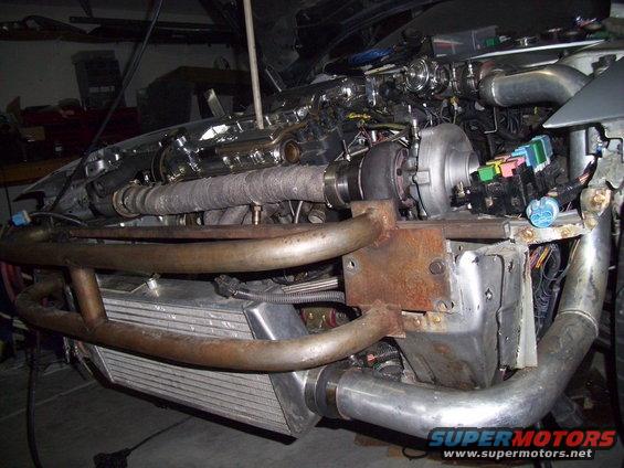 Engine bay with turbocharger, intercooler, and exhaust piping. Some wiring and a fuse box are visible