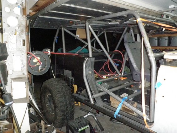 Interior view of a vehicle with a custom roll cage, large off-road tire visible