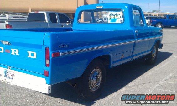 Blue Ford pickup truck, rear quarter view, white bumper, "Custom" badging