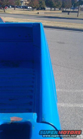 Blue pickup truck bed, showing chipped paint on the tailgate corner. The bed floor has visible ridges