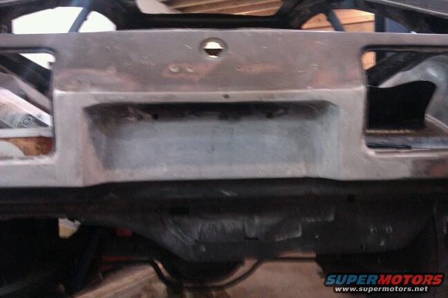 Rear of car under construction, showing unfinished metal panel and suspension components