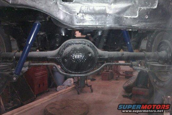 Rear axle assembly with blue shock absorbers, under a vehicle frame. Red tool chest visible