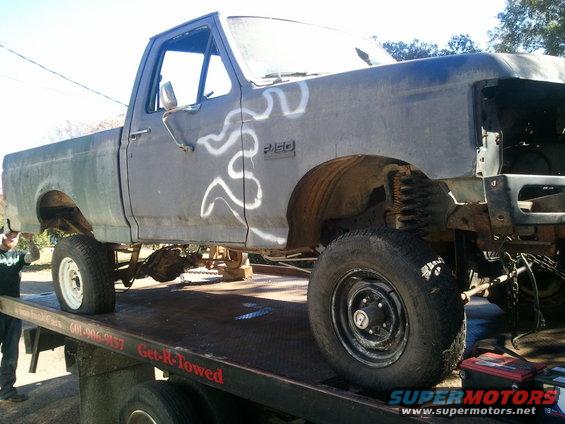 Old Ford F-350 pickup truck on a tow truck, missing front end, with white flame decals on the side