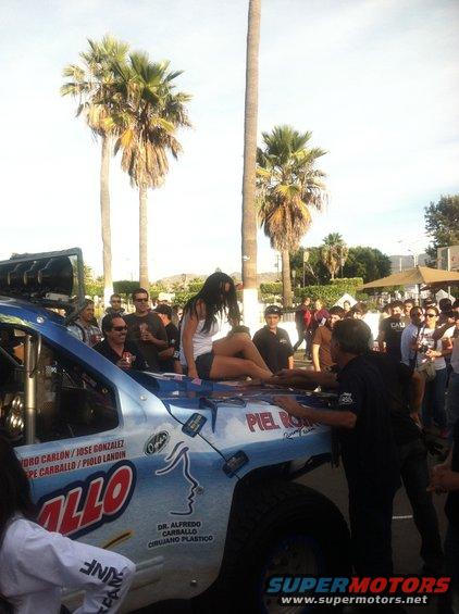 Light blue off-road truck with 'PIEL ROJA' and medical clinic text, woman on hood