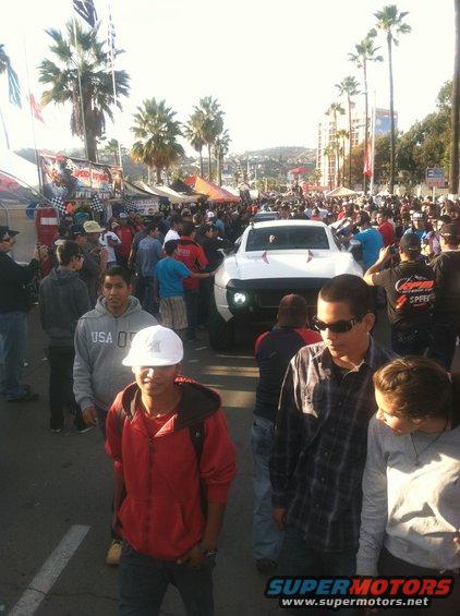White pickup truck with custom headlights and grille, surrounded by crowds at an outdoor event