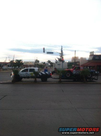 White pickup truck towing a red and blue race truck on a trailer