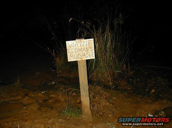 Sign reading Wayne Redman's Mud Hole in a dark, muddy outdoor scene