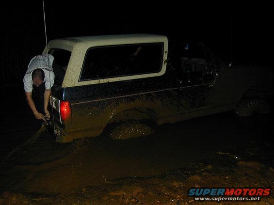 1996 Ford Bronco stuck in mud, person pulling a rope from the rear bumper