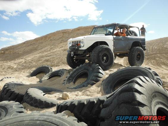 White and gray off-road vehicle with large tires on a sandy hill, surrounded by old tires