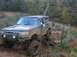 1996 Ford Bronco - This lifted SUV is navigating a challenging off-road trail covered in mud and rocks.