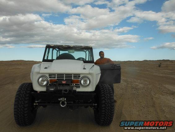 White Ford Bronco with winch and aftermarket wheels, driven by a man in an orange shirt