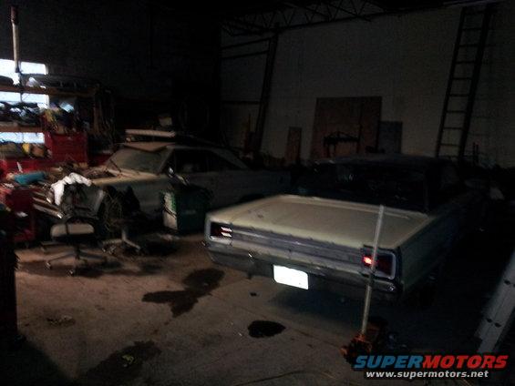 Rear view of a light-colored classic car with a dark car behind it in a garage